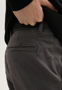 Gray woven trousers with a textured finish, featuring a back pocket and belt loops, worn with a black sweater covering the waistband.