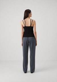 Top negro ajustado con tirantes finos y espalda plana, combinado con pantalones de pierna ancha grises que cuentan con un bolsillo lateral y una textura suave.