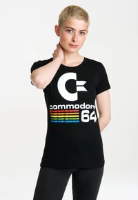 Black cotton t-shirt featuring a large white "C" logo and "commodore 64" in white, with colorful horizontal stripes in red, yellow, and blue.