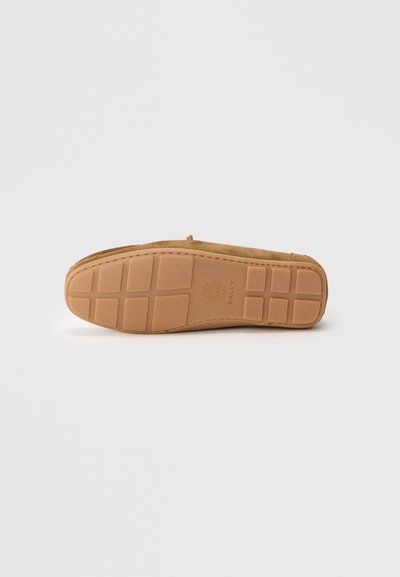 Hnědé semišové slip-on boty s gumovou podrážkou s vzorovaným gripem. Podrážka má otisk loga a výrazný design panelů.