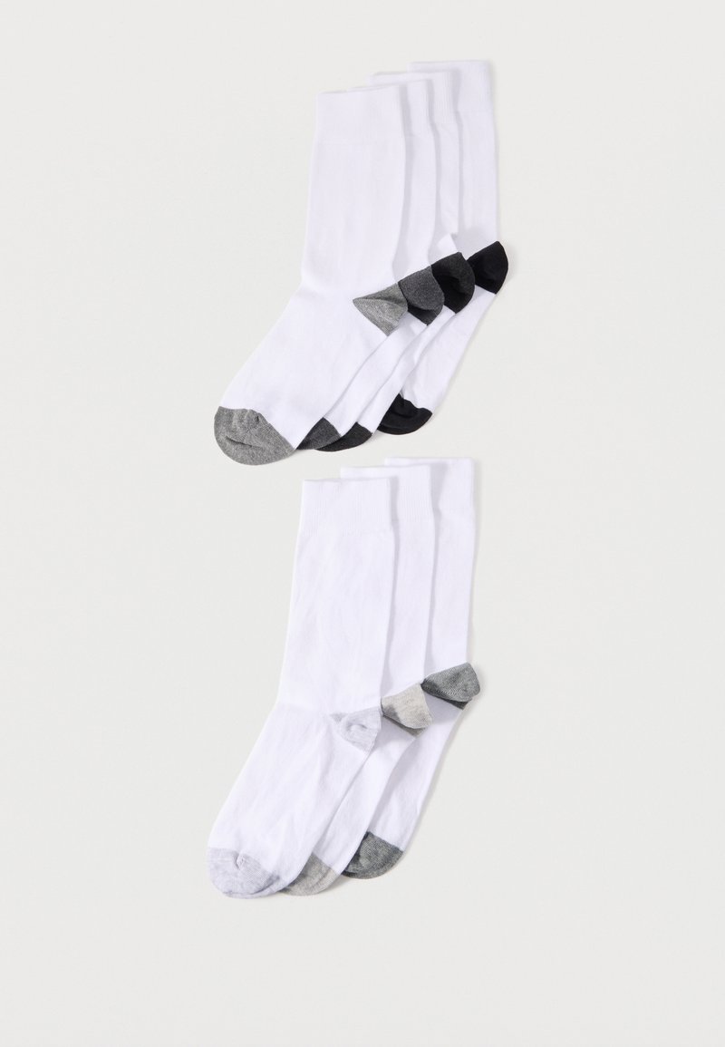 Deux paires de chaussettes blanches montantes avec des bouts et talons renforcés gris et noirs, disposées en piles chevauchantes sur un fond uni.