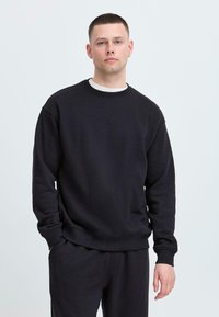 Felpa nera realizzata in tessuto morbido, con collo rotondo, maniche lunghe e polsini e orlo a costine. Vestibilità casual e design minimalista.