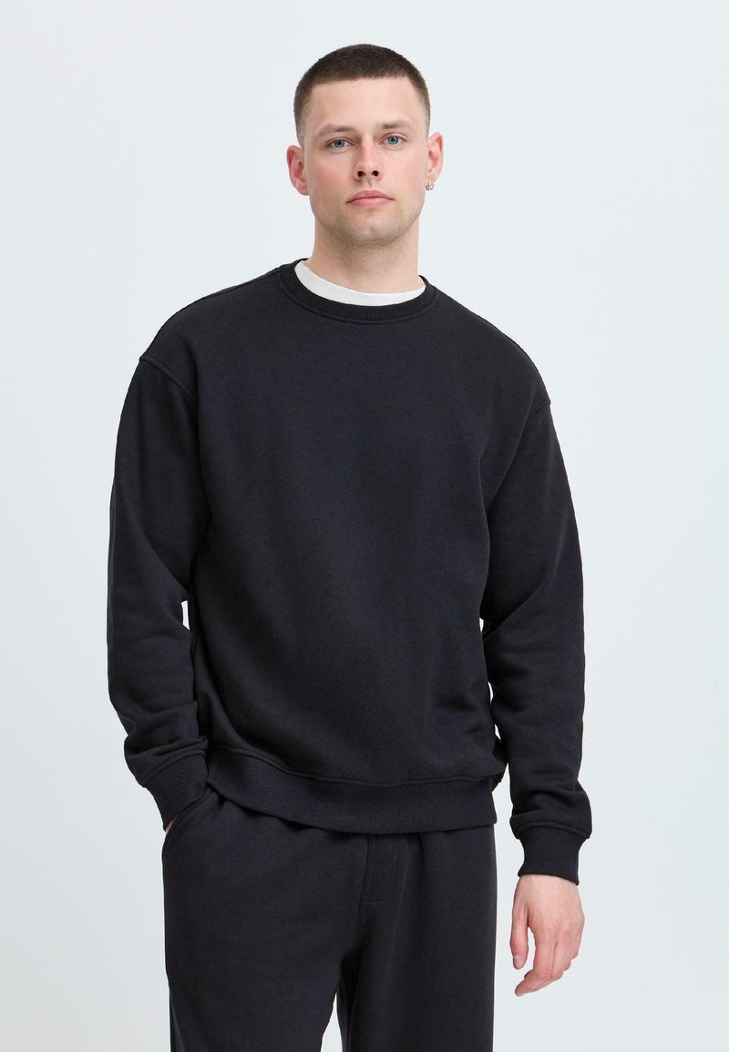 Felpa nera realizzata in tessuto morbido, con collo rotondo, maniche lunghe e polsini e orlo a costine. Vestibilità casual e design minimalista.
