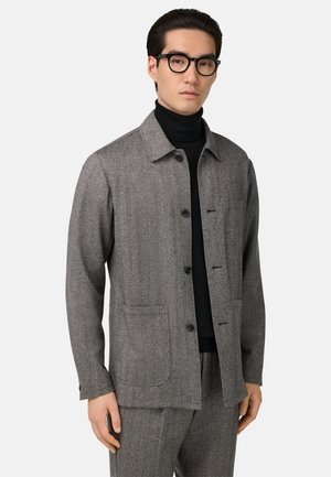 Gray wool-blend jacket with a collar, button closures, and two front pockets. Worn over a black turtleneck, featuring a textured finish.