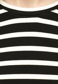 Primo piano del colletto di una maglietta a righe orizzontali bianche e nere che mostra la trama del tessuto e i dettagli delle cuciture.