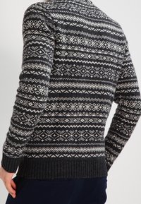 Suéter de punto oscuro con un patrón Fair Isle en blanco y gris, dobladillo acanalado, mangas largas y escote redondeado.