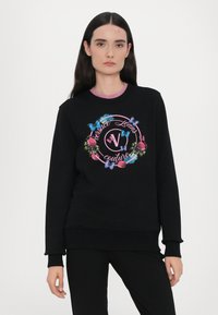 Čierna mikina s grafickým motívom kvetov a motýľa, na ktorej je text "Versace Jeans Couture" v ružovej farbe. Vyrobená z bavlny s rebrovanými manžetami.