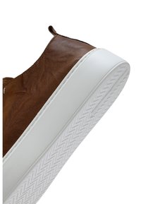 Bruine leren instapsneaker met dikke witte rubberen zool en gestructureerd zigzagprofiel op de buitenzool.