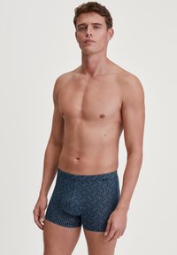 Donkerblauwe zwembroek met een geometrisch patroon in lichtblauw, gemaakt van elastisch materiaal, met een aansluitend ontwerp en een lengte tot het midden van de bovenbenen.