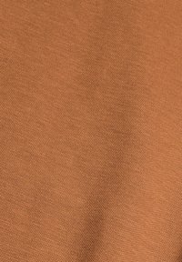 Zbliżenie na teksturowany pomarańczowy materiał z małym, równomiernie rozłożonym wzorem tkanym i delikatnym cieniem tworzącym subtelną krzywiznę.