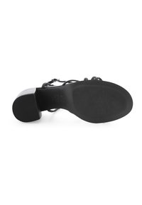 Schwarze Sandale mit Absatz, die eine strukturierte Gummisohle, ein träger Design und einen Blockabsatz aufweist. Die Riemen bestehen aus glattem Material.