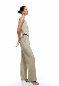 Top corto de textura beige con botones, combinado con pantalones de pierna ancha. Los pantalones cuentan con una cinturilla elástica y bolsillos laterales. Usado con sandalias.