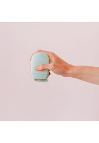 Envase de crema de manos en verde menta sostenido en una mano. Diseño ovalado y suave con tapa abatible y logotipo en relieve en la parte frontal.