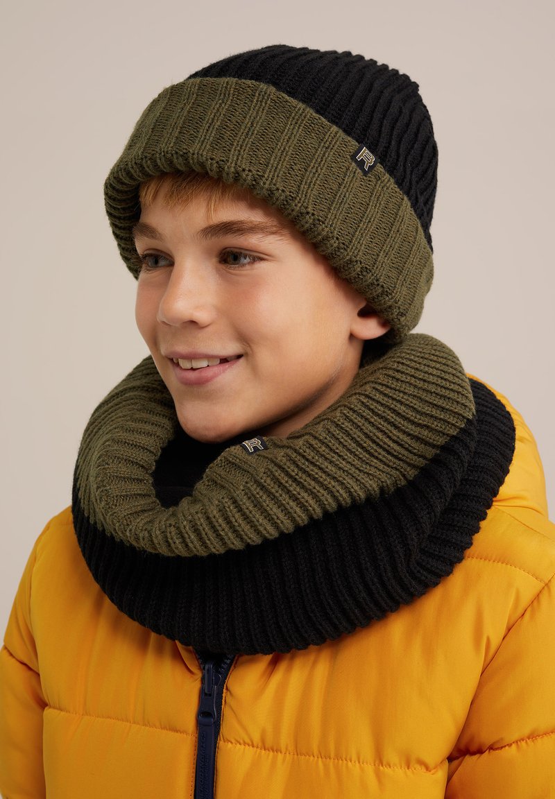 Stickad mössa och matchande halsduk i olivgrön och svart. Halsduken har en bred ribbad textur. Klart gul puffjacka i bakgrunden.