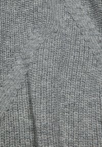 Primo piano di un tessuto grigio lavorato a maglia con un motivo a coste verticali e dettagli a treccia diagonale.