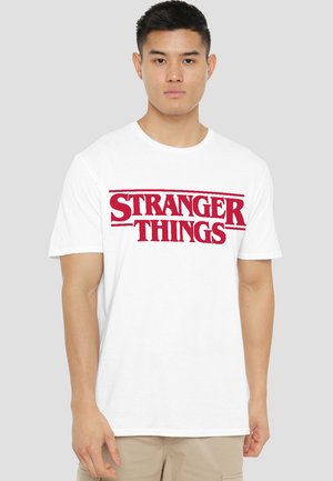 White cotton t-shirt featuring bold red "STRANGER THINGS" graphic text across the chest. Short sleeves, crew neck design.