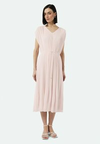 Faltendes rosa Midi-Kleid mit V-Ausschnitt, kurzen Ärmeln und einem Kordelzug an der Taille. Kombiniert mit weißen Riemchensandalen.