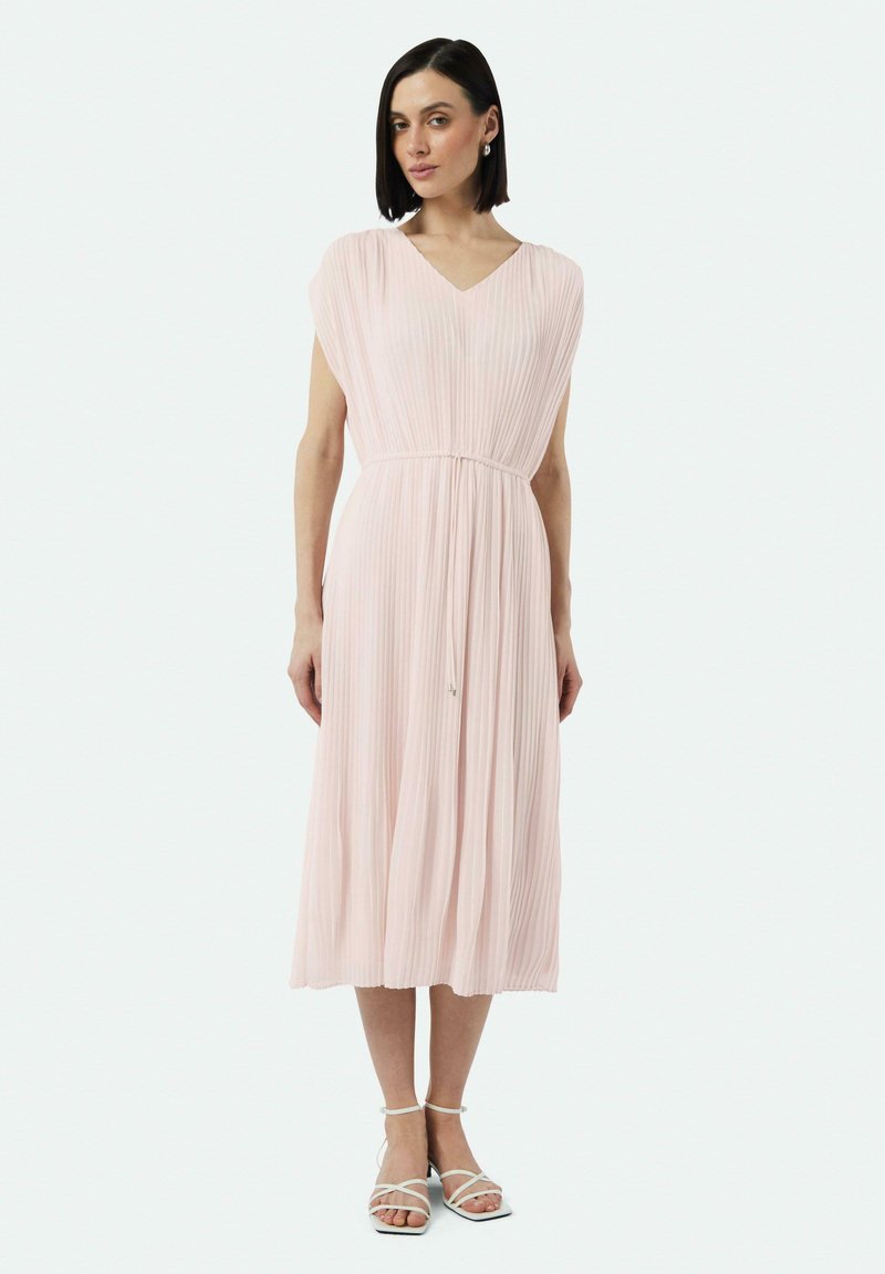 Faltendes rosa Midi-Kleid mit V-Ausschnitt, kurzen Ärmeln und einem Kordelzug an der Taille. Kombiniert mit weißen Riemchensandalen.