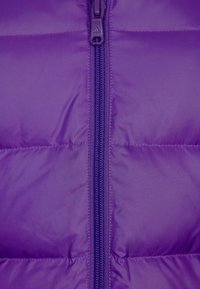 Doudoune violette avec panneaux matelassés, fermeture éclair centrale et texture lisse. Le tire-zip est marqué et assorti en violet.