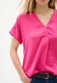 Blusa fucsia con scollatura a V e maniche corte, realizzata in un tessuto morbido; presenta drappeggi sottili e una vestibilità fluida.