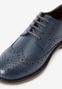 Scarpa oxford in pelle blu navy con dettagli brogue, lacci grigi e una texture liscia, punta arrotondata e suola robusta.