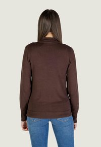 Brązowy sweter z dzianiny z ribbowanym dolnym wykończeniem i mankietami, charakteryzujący się klasycznym krojem. W zestawie z niebieskimi dżinsami, widok z tyłu.