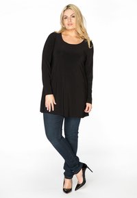 Schwarze Langarm-Tunika mit Rundhalsausschnitt, kombiniert mit dunkelblauen Skinny Jeans und schwarzen hohen Schuhen. Glatter Stoff, lockere Passform.