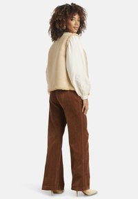 Beige faux fur vest over a white embroidered long-sleeve top, paired with brown corduroy wide-leg pants and nude heels.