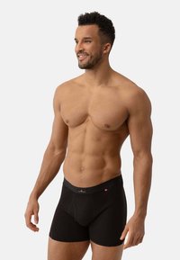 Zwarte boxershorts gemaakt van zachte stof, met een soepele tailleband en een gesloten pouch ontwerp, getoond op een mannelijke model met een neutrale achtergrond.