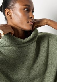 Maglione verde a maglia con colletto alto ripiegato; la sua texture è morbida e leggermente costata. Presenta una vestibilità comoda e si adagia delicatamente sulle spalle.