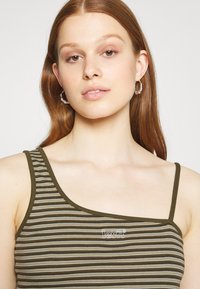 Top de alças com riscas em verde-oliva e bege, com um design de um ombro. Apresenta alças finas e o logo bordado "levi's" no peito.