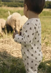 Beige overall med brunt nallebjörnstryck, långa ärmar och knappstängning längs sidan, designad för små barn.