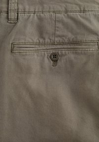 Beige Stoff mit einer subtilen diagonalen Textur, der eine Gesäßtasche aufweist, die mit einem Vier-Knopf-Verschluss gesichert ist.