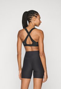 Svart sports-bh med kryssryggdesign og utskjæringsdetaljer, kombinert med høyt liv svarte shorts, som fremhever et jevnt, teksturert stoff.