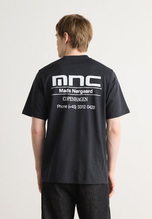 Black cotton t-shirt featuring large white text on the back, including "mnc," "Mads Nørgaard," "COPENHAGEN," and a contact number.