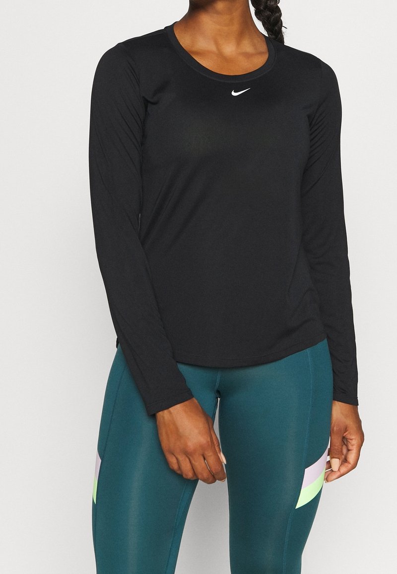 Langärmliges schwarzes Sportoberteil mit Rundhalsausschnitt und Nike-Logo auf der Brust, kombiniert mit türkisfarbenen Leggings mit bunten Streifenakzenten.
