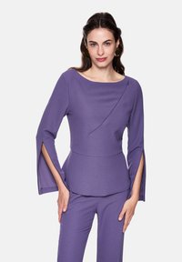 Purple long-sleeve top with a boat neckline, featuring side slits on sleeves and a diagonal seam detail. Smooth, textured fabric.