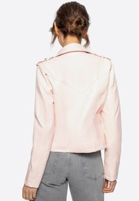 Chaqueta de piel sintética de color rosa claro con hombros estructurados, corte entallado y costuras blancas en contraste. Presenta un diseño de yugo trasero en ángulo.