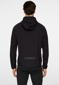 Svart lättviktsjacka med huva, elastiska ärmslut och en ficka med dragkedja på baksidan, tillverkad av ett slätt, hållbart tyg.