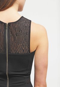 Schwarzes Kleid mit einem strukturierten, transparenten Rückenteil mit geometrischem Muster, Reißverschluss und nahtlosem Design an der Taille.