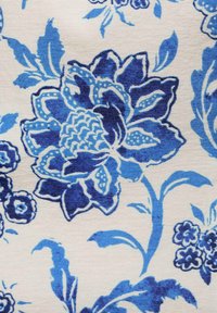 Blommig tyg med stora blå rosor och mindre blommor på en krämfärgad bakgrund. Designen inkluderar detaljerade kronbladsmönster och blad.