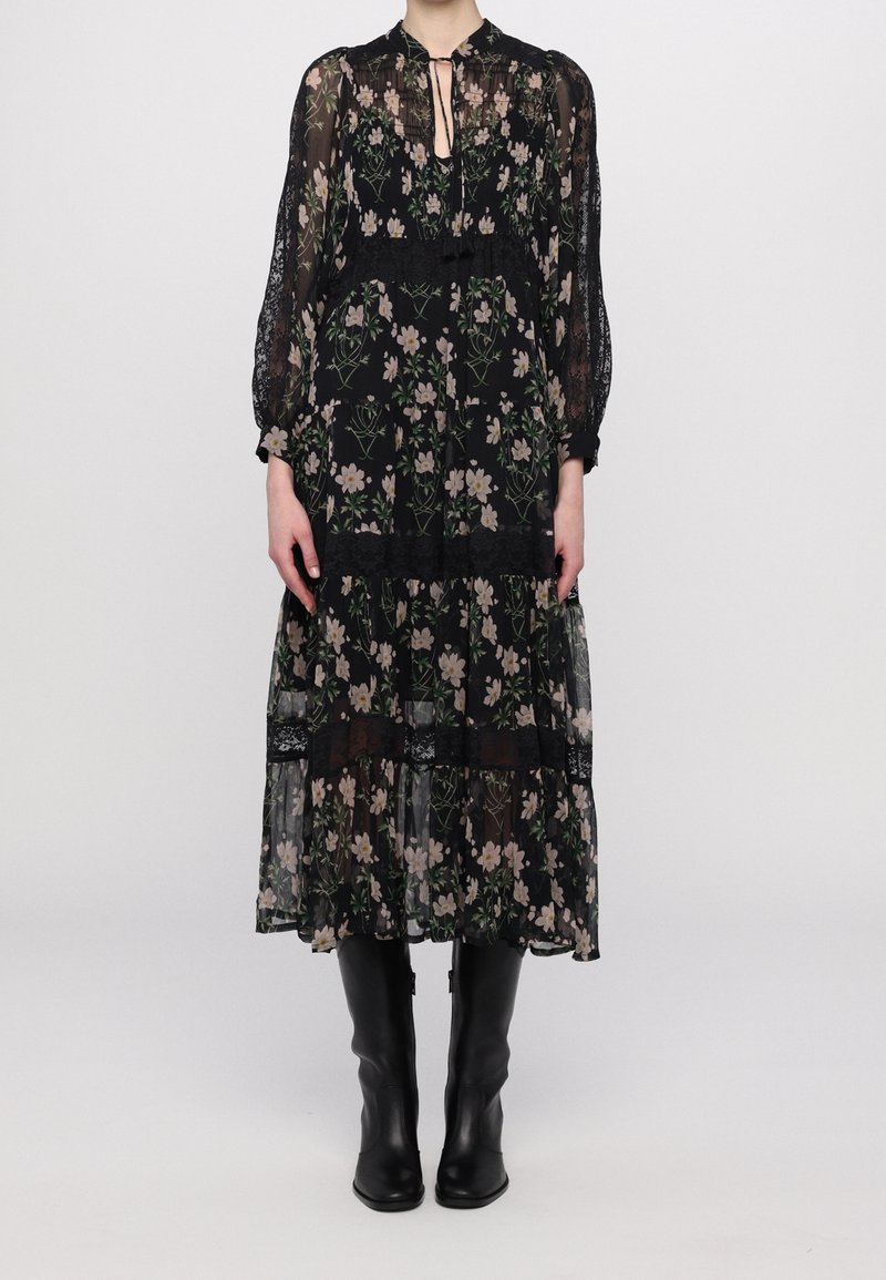 Robe maxi noire transparente avec imprimé floral, dotée de manches longues, d'un col haut avec une ouverture en forme de goutte, et d'accents en dentelle sur les volants. Bottes noires jusqu'aux genoux.