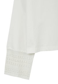 Camicia bianca a maniche lunghe con un polsino in pizzo all'uncinetto testurizzato con un motivo floreale. Tessuto di cotone morbido con una vestibilità rilassata.