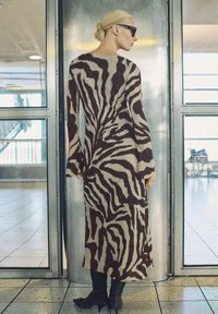 Long-sleeved dress featuring a zebra stripe pattern in brown and cream, made of soft fabric, with a fitted silhouette and flowing design.