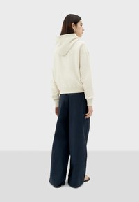Cream-colored, cropped hoodie with a hood, paired with wide-leg navy blue pants. Smooth fabric with minimal seams and no visible patterns.