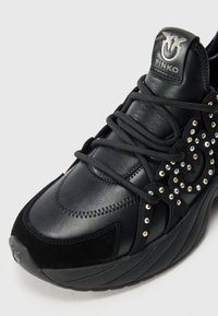 Zwarte sneaker gemaakt van een combinatie van leer en suède materialen, met ingewikkelde stiksels en versieringen van strass in verschillende kleuren.