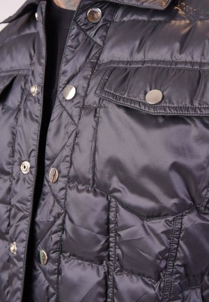 Giacca nera imbottita con design trapuntato, dotata di bottoni a pressione argentati e due tasche frontali. Tessuto liscio con colletto e cerniera.