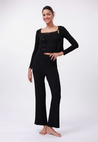 Sort lounge-sæt bestående af en langærmet cardigan med knapper og en cropped tanktop med blonder, kombineret med bukser med vide ben.