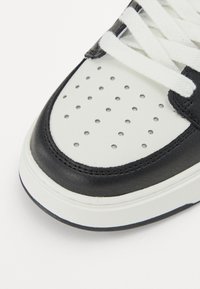 Schwarzer und weißer Sneaker mit glattem Lederobermaterial, perforierter Zehenbox und weißen Schnürsenkeln. Verfügt über eine gepolsterte Sohle und dezente Stichdetails.
