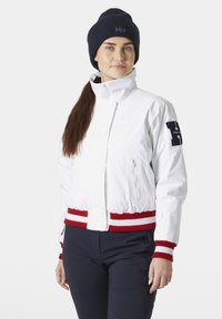 Bílá bomber bunda s červeným a bílým pruhovaným ribbed akcentem v pase, s kapsou na zip a námořnickou pletenou čepicí.